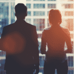 A man and woman are silhouetted looking out a window on a city scape.