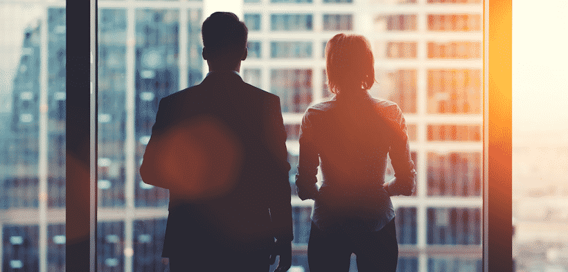 A man and woman are silhouetted looking out a window on a city scape.